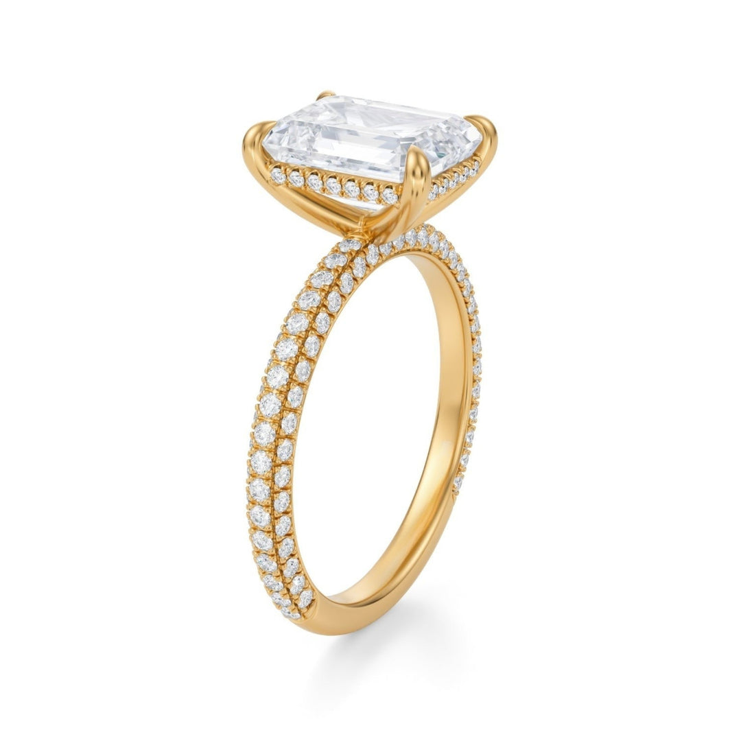 An emerald cut diamond ring with a halo and pave band, set in a mounting, with a white background.